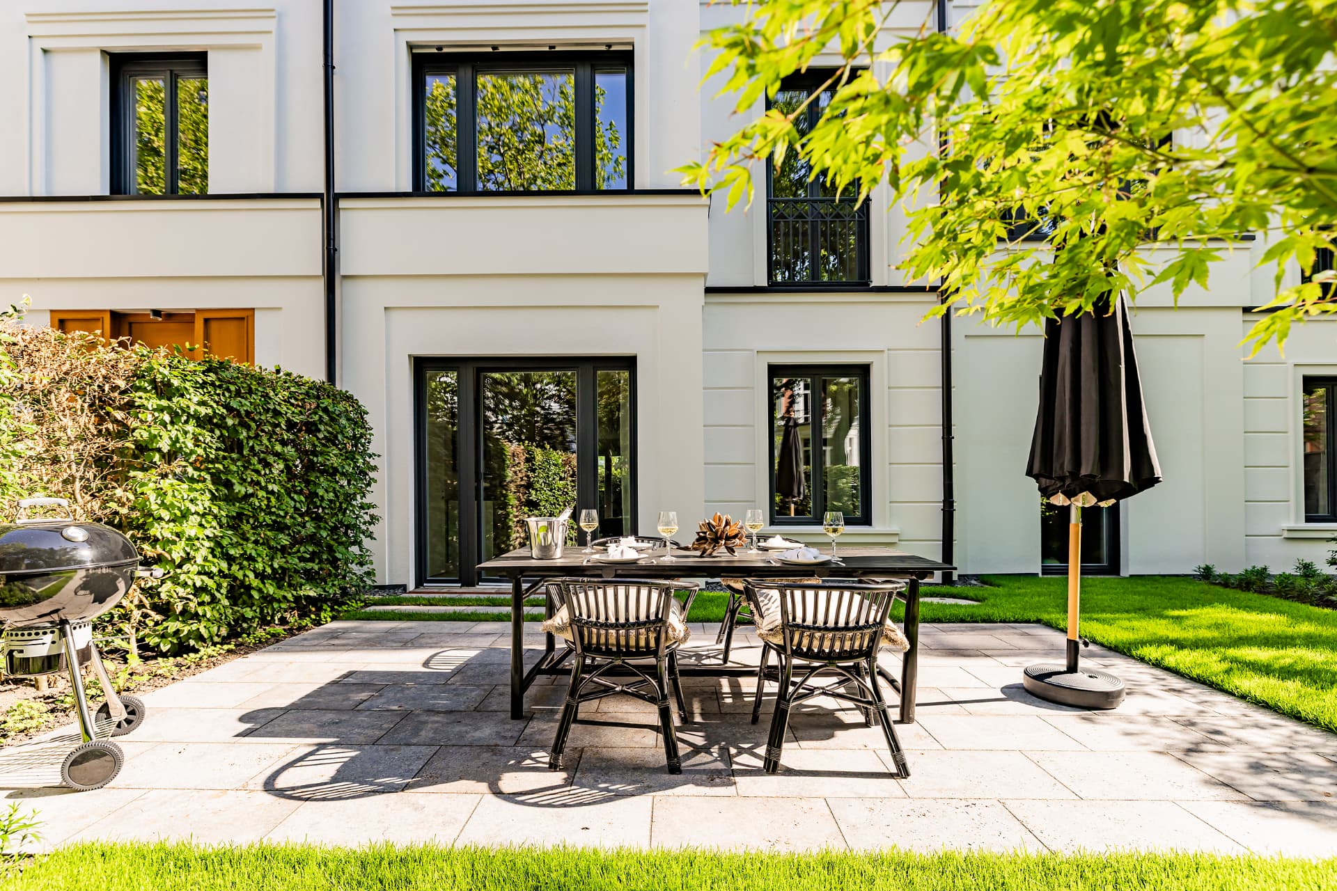 Essplatz auf der Natursteinterrasse vor den bodentiefen Fenstertüren der Stadtvilla